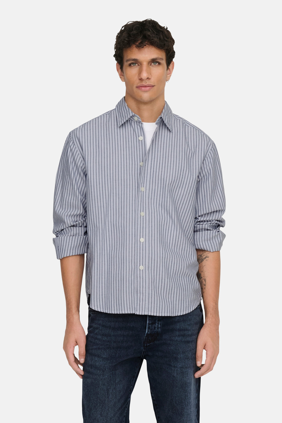 Chemise rayée bleue à longues manches de ONLY & SONS®, avec des manches retroussées, associée à des jeans foncés et des chaussures noires.