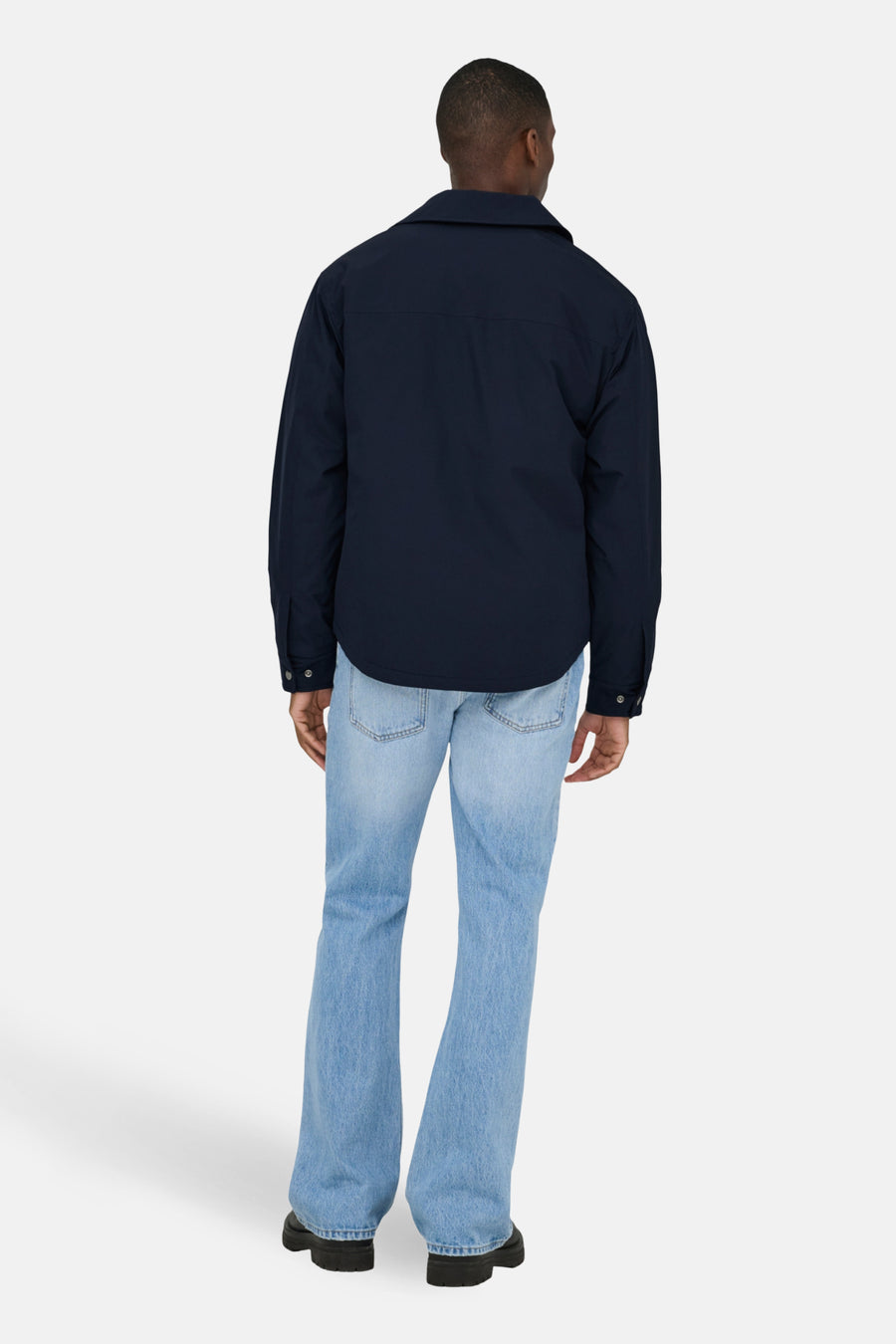 Persoon van achteren gezien, marineblauwe jas, blauwe spijkerbroek, zwarte schoenen.