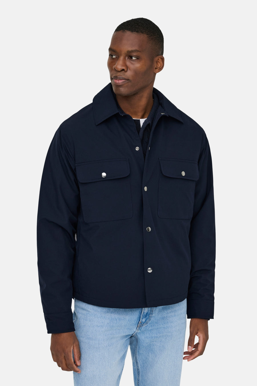 Man in blauwe jas met zilveren knopen en lichte jeans.