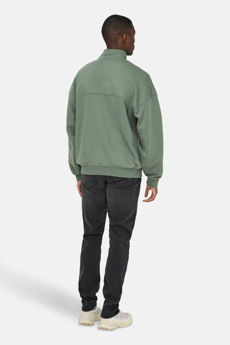 Man in olijfgroene trui en zwarte jeans, van achteren gezien.