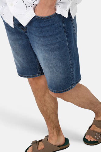 Short en jean de couleur bleu moyen de ONLY & SONS®, porté par un homme avec une main dans la poche, un haut blanc et des sandales marron avec une semelle intérieure verte.