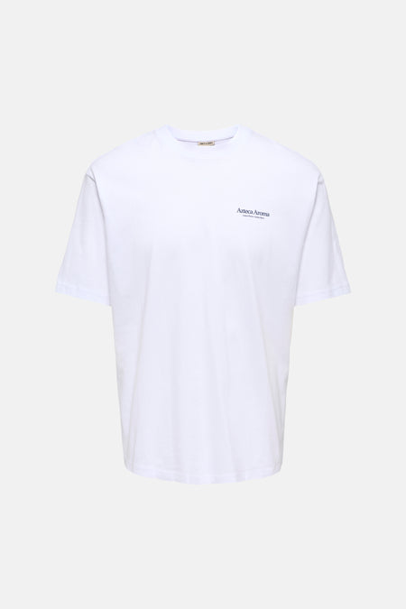 T-shirt blanc à manches courtes ONLY & SONS®, avec un imprimé coloré de fleurs et de têtes au dos, porté avec un jean foncé et des baskets blanches.