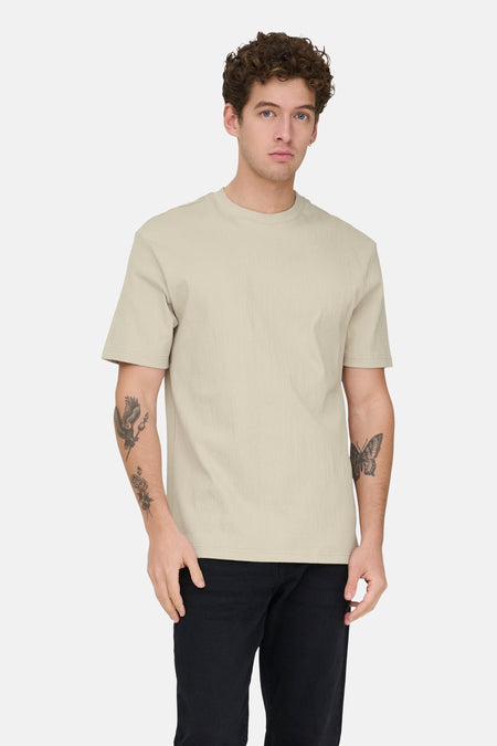 T-shirt écru à manches courtes ONLY & SONS®, uni avec une texture subtile, porté avec un jean noir et des baskets.