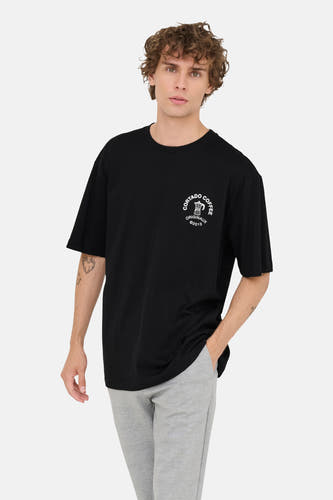 T-shirt noir à manches courtes de ONLY & SONS®, avec une impression blanche et porté avec un pantalon gris.