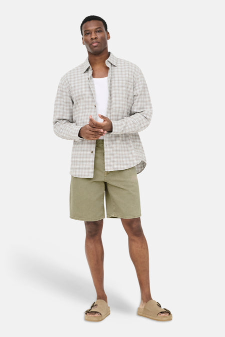 Beige jeansshort van ONLY & SONS, gedragen door een man met open geruit overhemd en sandalen.