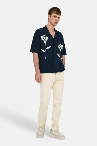 Blauwe pull van ONLY & SONS® met korte mouwen en wit bloemenpatroon, gedragen met crèmekleurige broek en sneakers.
