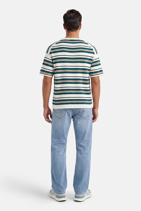 Crème, groen, bruin en zwart gestreepte T-shirt van ONLY & SONS®, achterkant op een man met lichtblauwe spijkerbroek en grijze sneakers.