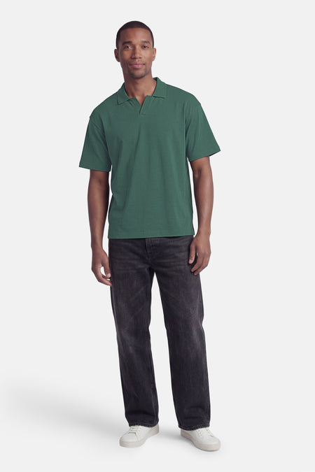 Polo verte ONLY & SONS® de couleur verte avec col en V et manches courtes, portée par un homme avec un jean noir et des baskets blanches.