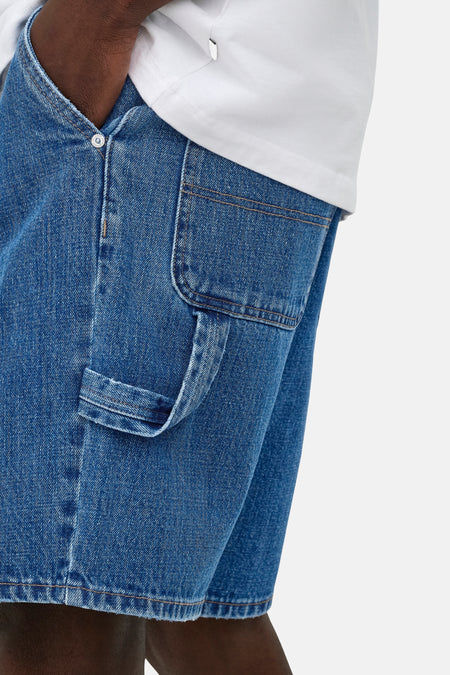 Short en jean bleu moyen de ONLY & SONS® avec poche carpenter et passant à outils, porté avec un t-shirt blanc.