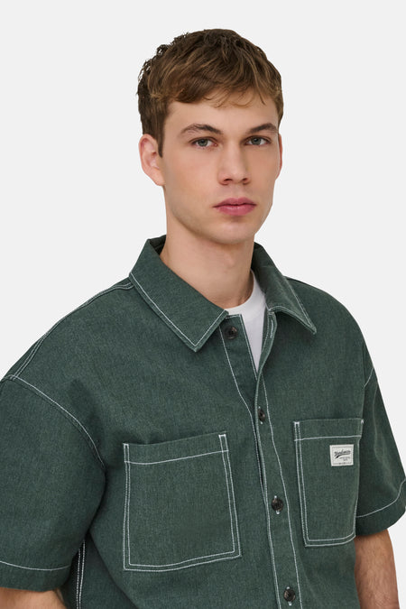 Chemise verte à manches courtes de ONLY & SONS® avec surpiqûres blanches et poches poitrine, portée par un homme.