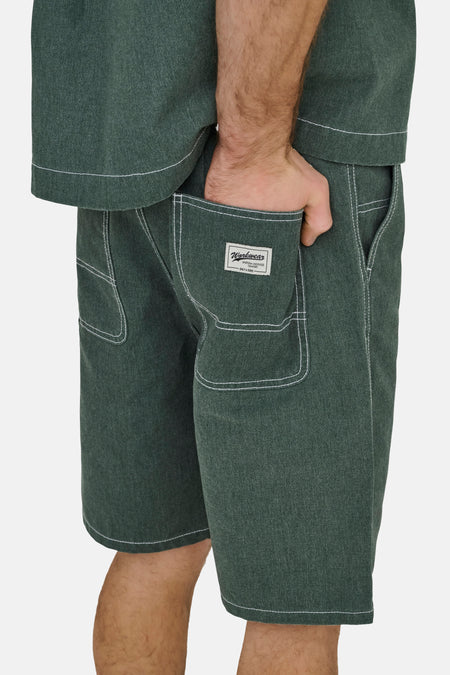 Short vert de ONLY & SONS® avec surpiqûres contrastées blanches, une texture et une étiquette sur la poche arrière, porté avec la main dans la poche.