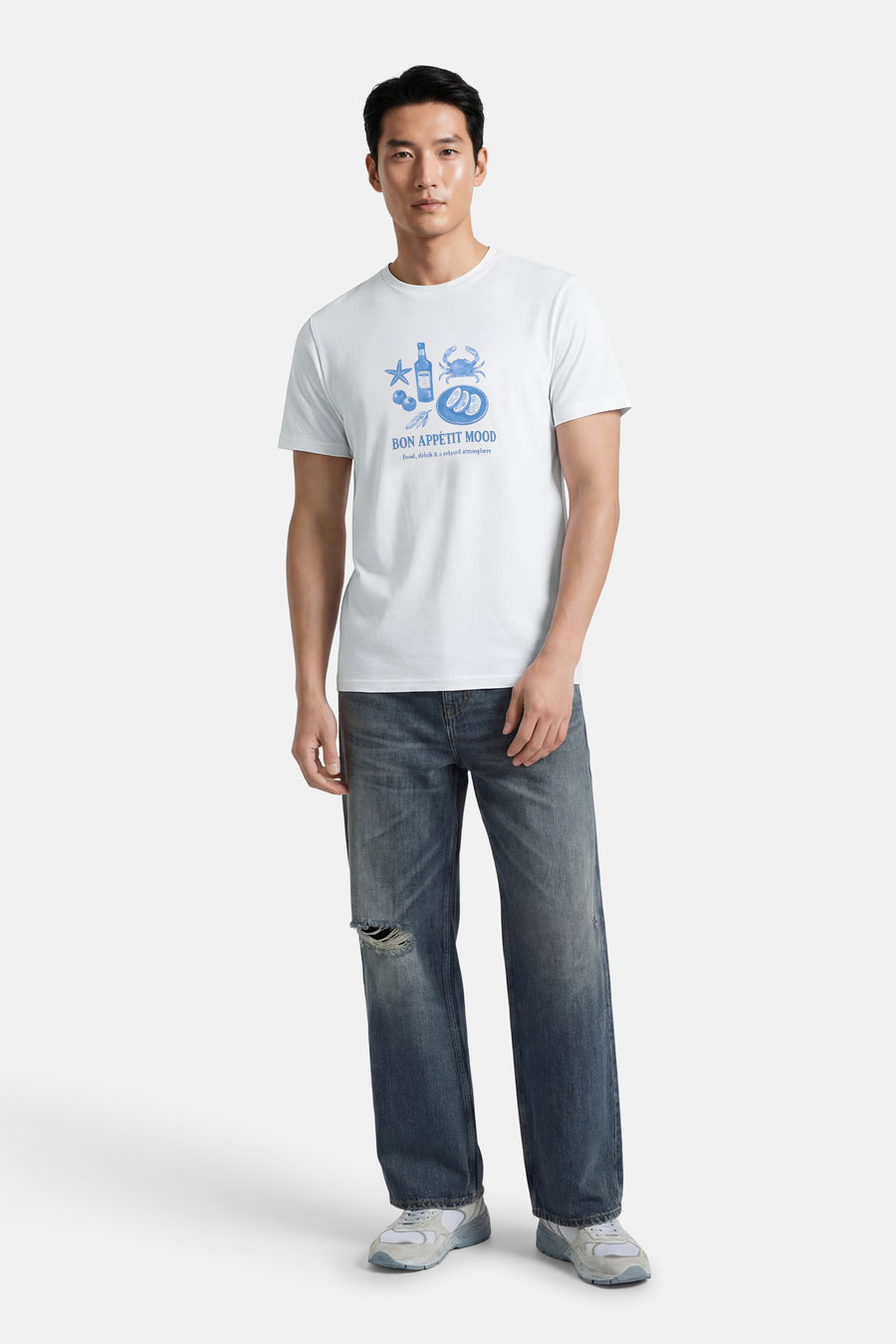 Wit T-shirt met korte mouwen van ONLY & SONS® met blauwe prints, gedragen met gescheurde jeans en sneakers.
