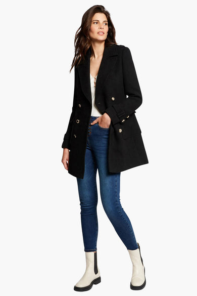 Un manteau de laine noire avec des jeans bleus et des bottes blanches.