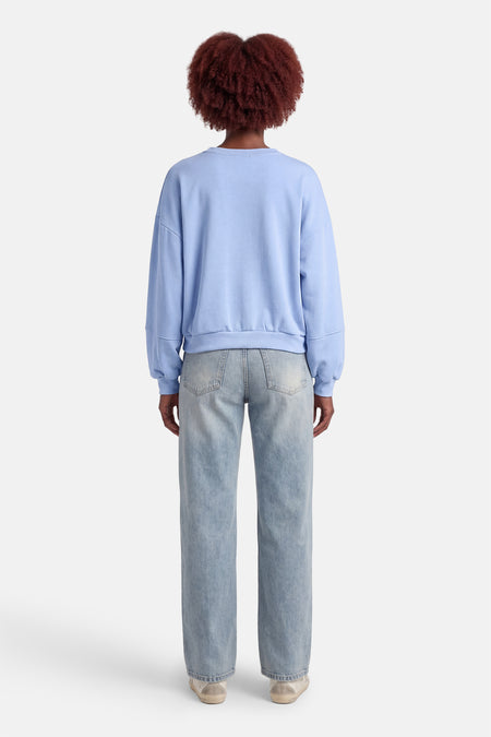 Pull bleu à col rond de Terra di Siena, vu de dos, combiné avec un jean bleu clair et des baskets basses.