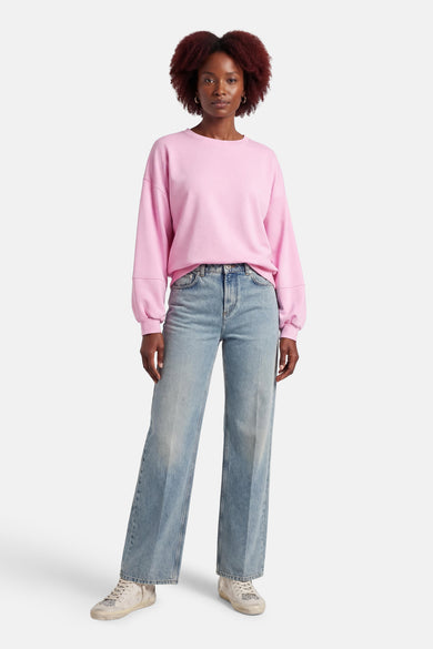 Pull rose de Terra di Siena, à manches longues, porté avec un jean ample et des baskets.