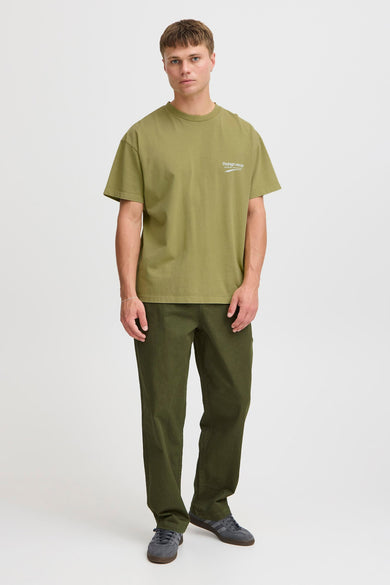 T-shirt vert avec manches courtes de THEJOGGCONCEPT, porté avec un pantalon vert et des baskets grises.