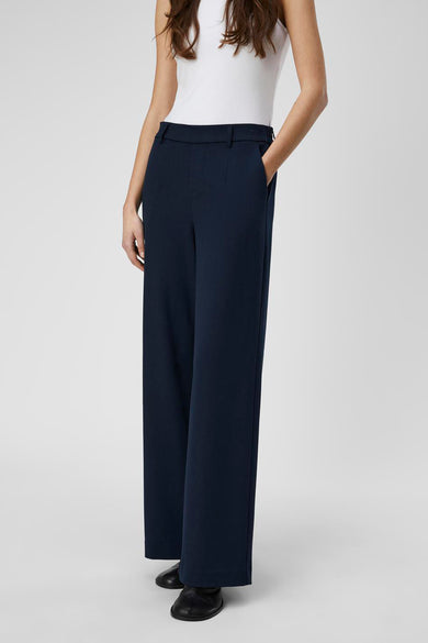 Pantalon bleu d'OBJECT, vu de l'arrière, avec une ceinture élastique et porté avec un tank-top blanc et des chaussures noires.