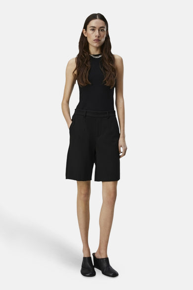 Short noir d'OBJECT, avec des boucles et porté avec une chemise noire et une chaîne argentée.