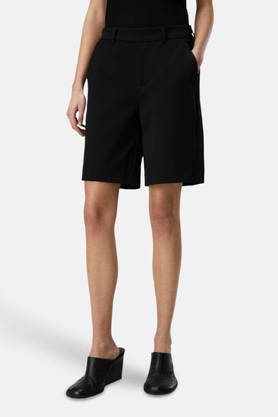 Short noir d'OBJECT, avec poches, combiné à une chemise noire et des bottes noires à talons.