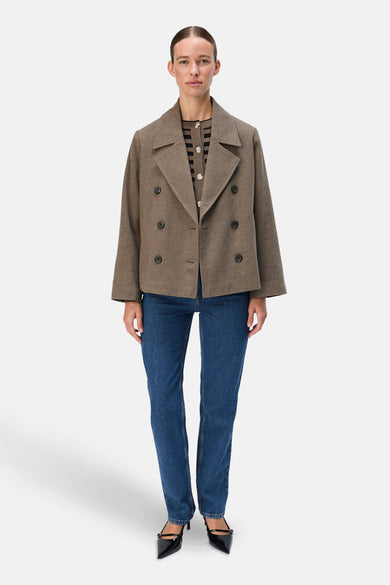 Manteau court brun d'OBJECT, avec une fermeture à double bouton et porté sur un cardigan rayé, avec des jeans bleus et des bottes noires.