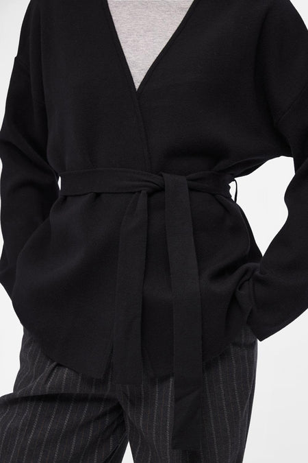 Gilet noir d'OBJECT avec une ceinture, porté sur un chemisier gris et un pantalon rayé.