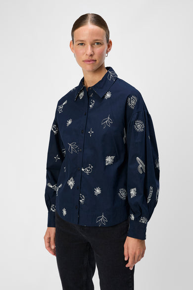 Chemise bleue à manches longues d'OBJECT, avec des imprimés blancs de divers motifs, associée à un jean noir et des baskets.