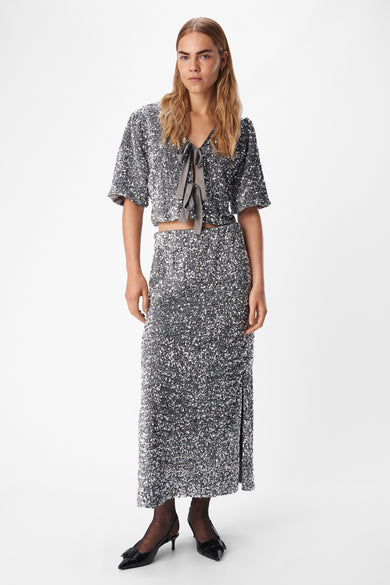 Long manteau argenté d'OBJECT, avec paillettes et une fente sur le côté, associé à des escarpins noirs et des bas.