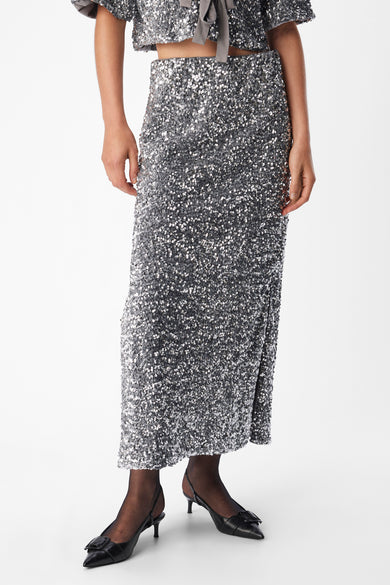 Long manteau argenté d'OBJECT, avec paillettes et une fente, porté avec des bas noirs et des chaussures.