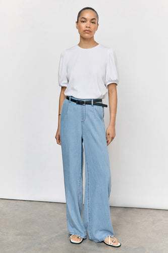 Vrouw in een witte top, wijde jeans met riem, en sandalen.