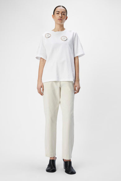 T-shirt blanc à manches courtes d'OBJECT, avec des motifs de fleurs tricotés sur les épaules, associé à un pantalon beige et des chaussures noires.