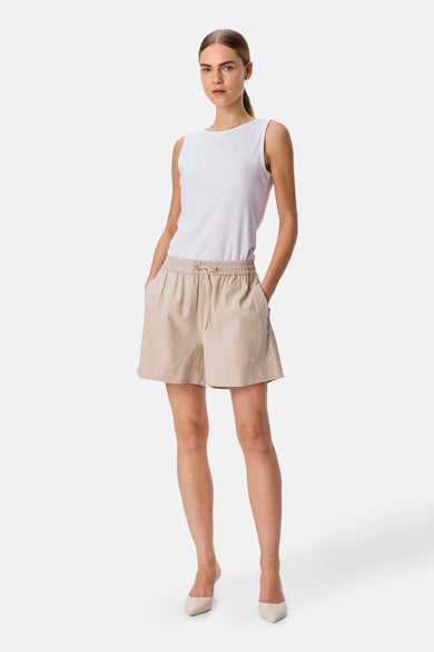 Crème court de OBJECT, avec une ceinture élastique et des poches, porté avec un chemisier blanc et des escarpins.