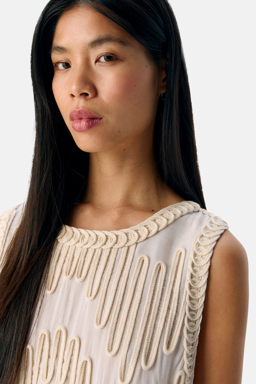 Vrouw in mouwloze, beige top met decoratief koordpatroon.
