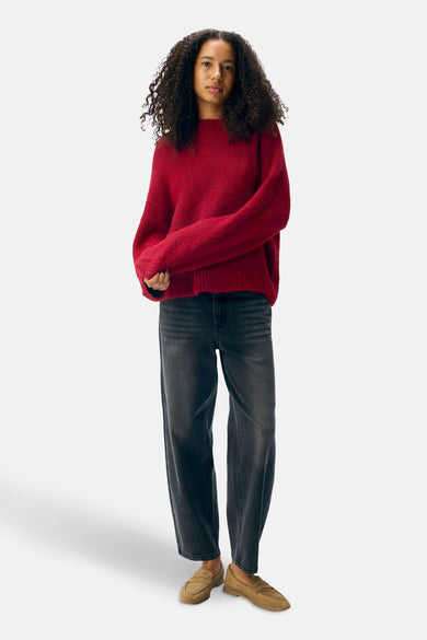 Femme en pull rouge, jeans gris et mocassins bruns.
