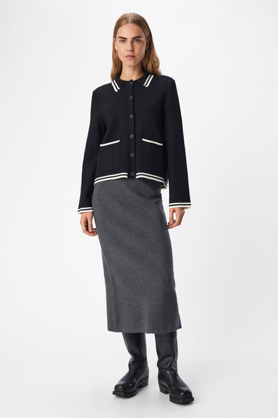 Cardigan noir d'OBJECT, avec des détails rayés blancs, associé à une jupe grise et des bottes noires.