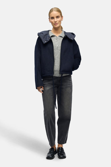 Manteau court bleu d'OBJECT, avec une capuche, associé à un pull gris, des jeans foncés et des chaussures noires.
