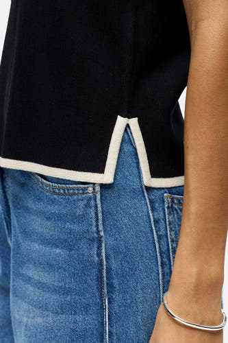 Haut sans manches noire de OBJECT avec passepoil blanc sur le bas, portée avec un jean et un bracelet argenté.
