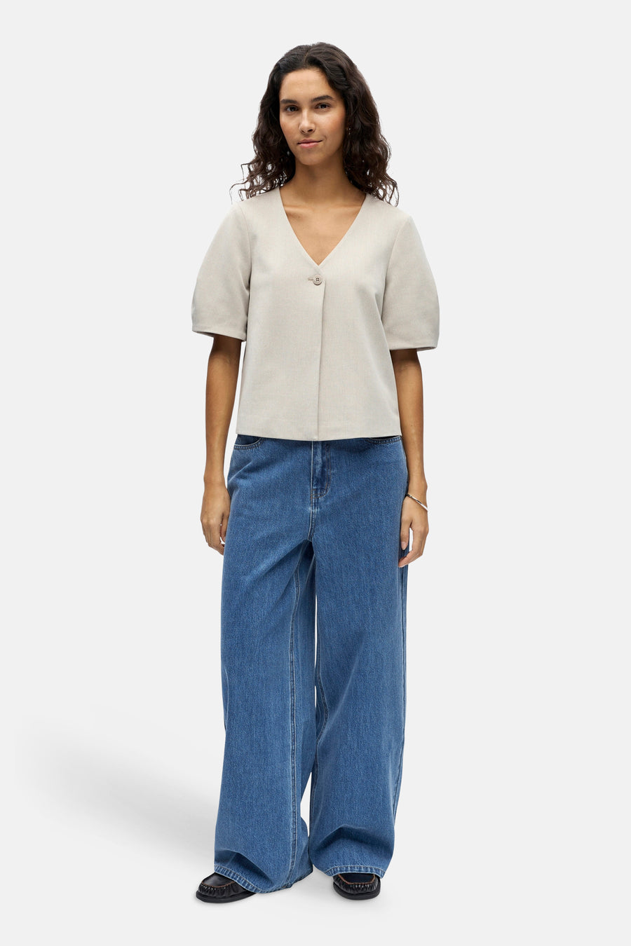 Gilet écru de OBJECT, avec fermeture à boutons, manches courtes et combiné avec un jean bleu large et des chaussures noires.