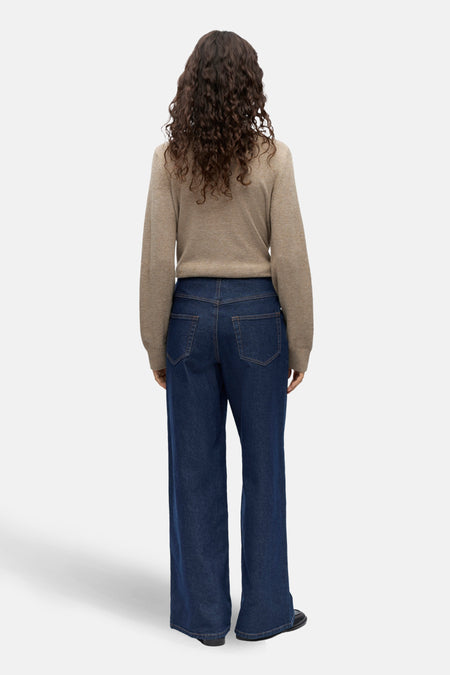 Vrouw, rugzijde, bruine trui, blauwe jeans, krullend haar.
