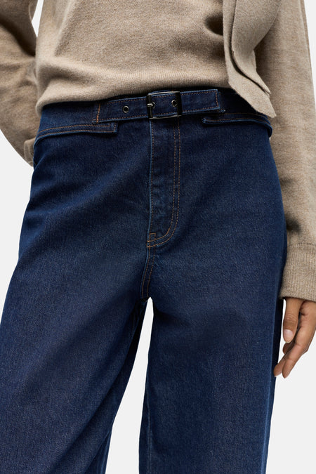 Donkerblauwe denim broek met ceintuur, beige trui.