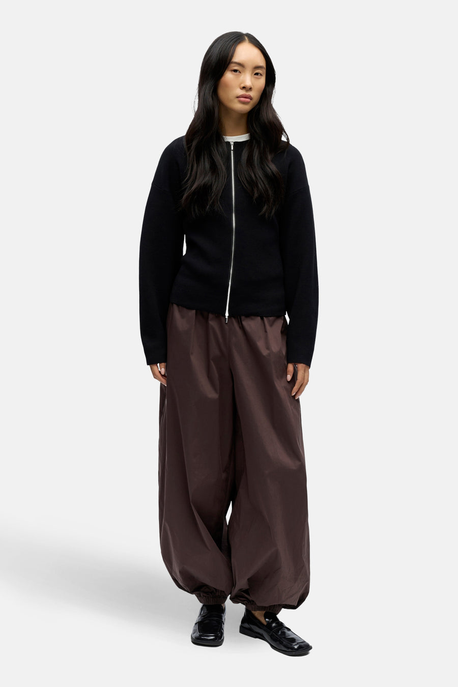 Vrouw draagt zwarte cardigan en bruine wijde broek.