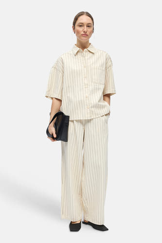 Chemise beige à manches courtes de OBJECT, avec rayures verticales et poche poitrine, stylisée avec un pantalon assorti, des mules noires et un sac à main.