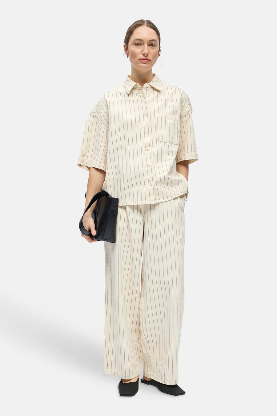 Chemise beige à manches courtes de OBJECT, avec rayures verticales et poche poitrine, stylisée avec un pantalon assorti, des mules noires et un sac à main.