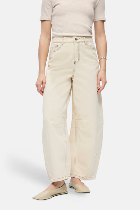 Jean beige coupe spéciale de OBJECT, à jambes larges, coutures contrastées, stylisé avec un t-shirt de couleur crème, un sac noué noir et des chaussures plates.