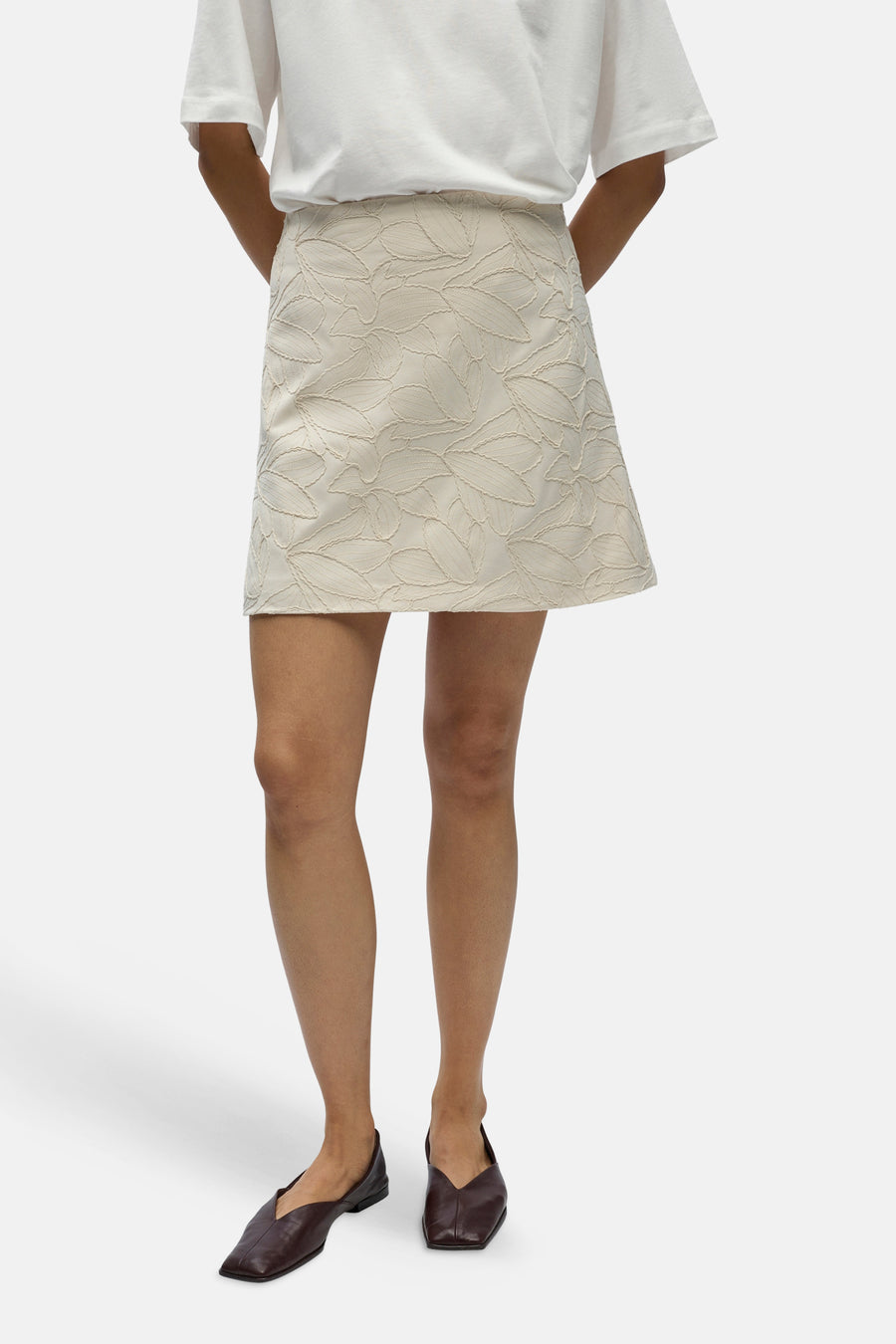 Jupe courte écru d'OBJECT, avec un motif de feuilles et combinée avec un t-shirt blanc et des chaussures plates marron.
