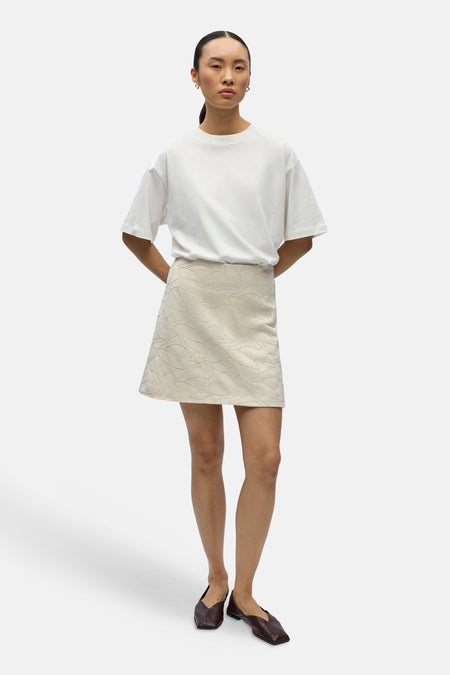 Jupe courte écru d'OBJECT, avec motif à feuilles et combinée avec un t-shirt blanc et des mocassins marron.