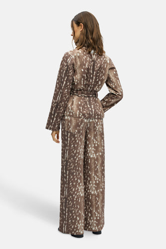 Vrouw in bruine broek en jas met stippen van achteren.