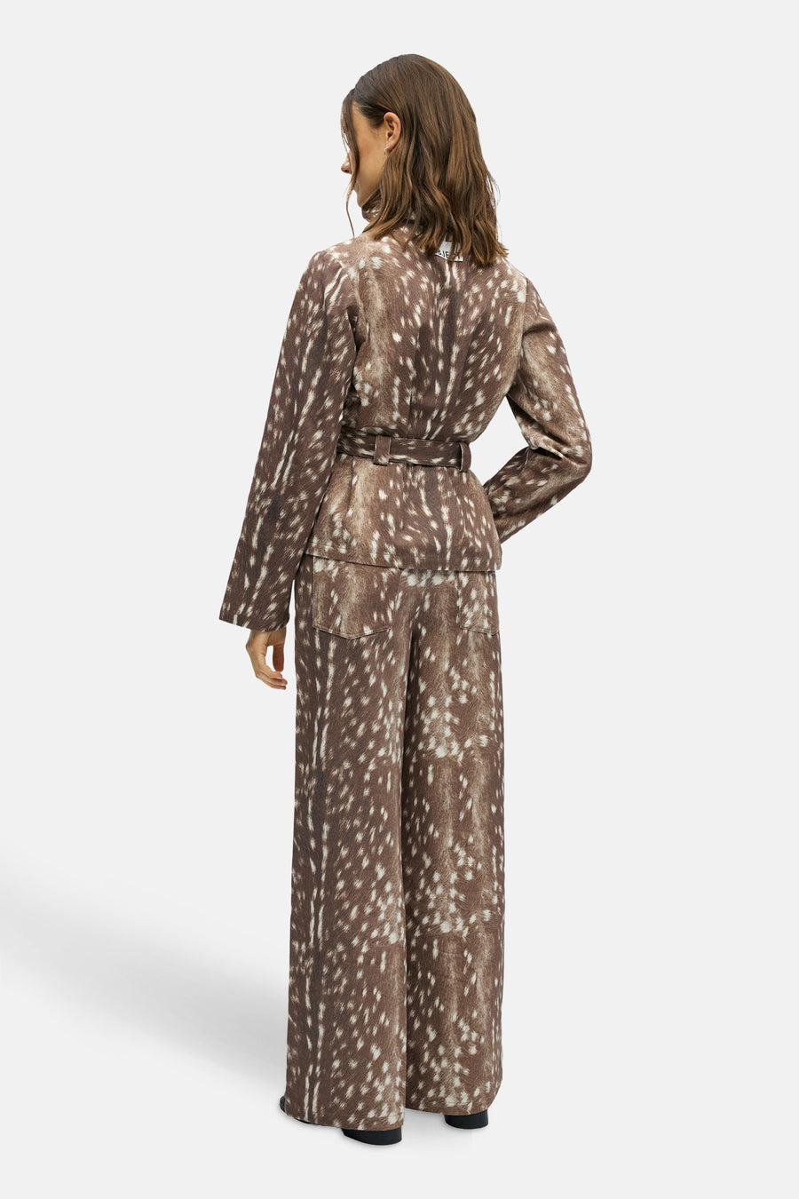 Vrouw in bruine broek en jas met stippen van achteren.