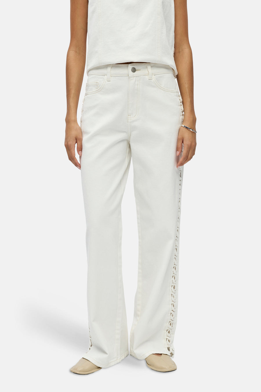 Jean blanc d'OBJECT avec détails découpés sur les côtés, stylisé avec un haut blanc, un bracelet argenté et des mules beiges.