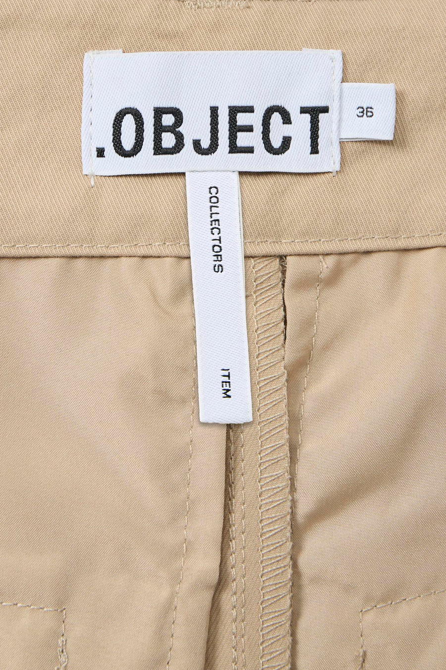 Pantalon beige de OBJECT avec une ceinture et une étiquette portant le texte ".OBJECT" et "COLLECTORS ITEM".