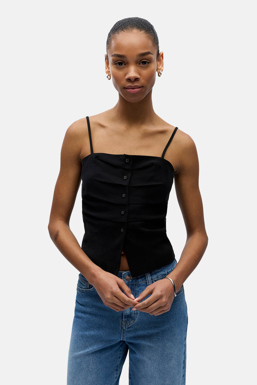 Haut noir à fines bretelles de OBJECT, avec fermeture à boutons et volants à l'avant, porté avec un jean bleu.